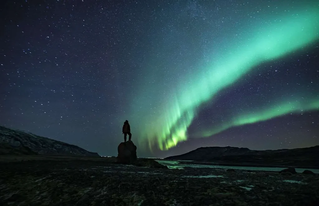 paesaggio notturno con uomo che ammira l'aurora boreale in Islanda