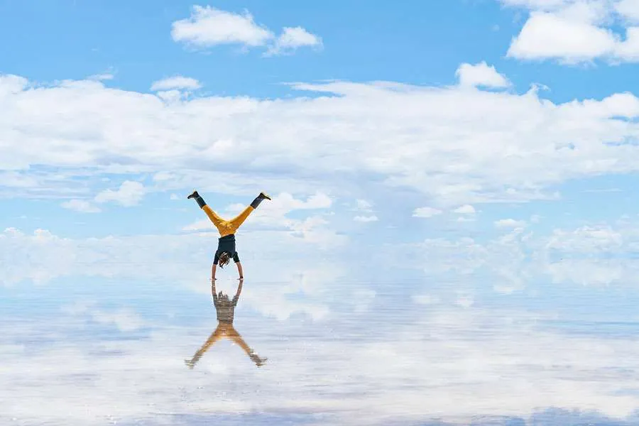 ragazzo che fa una verticale sullo scenario del cielo riflesso al salar de uyuni